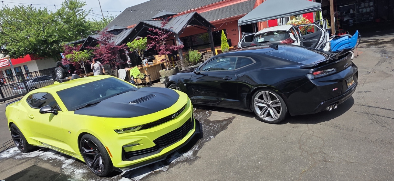 Two Chevrolet Camaros, one neon yellow and one black, outside Broadway Detailing in Portland