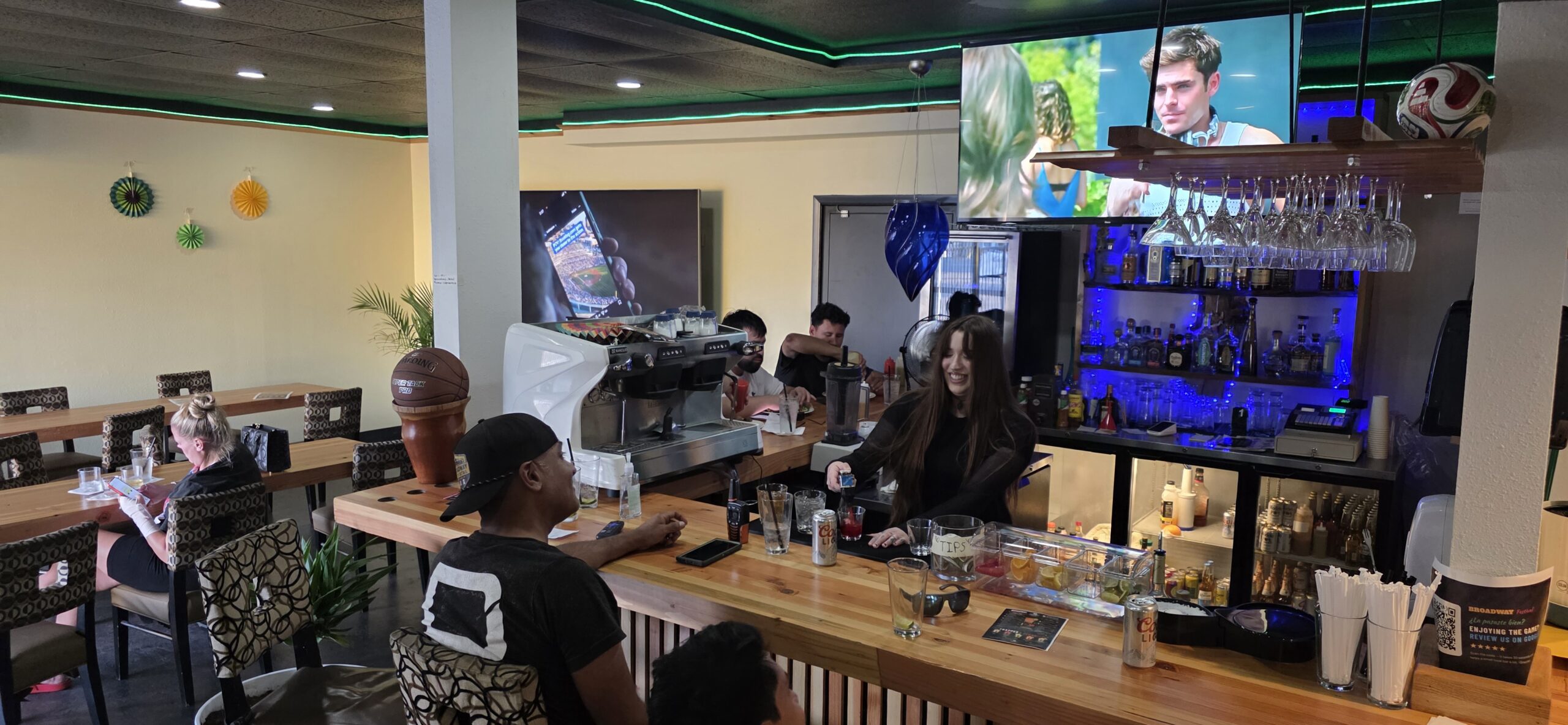 Interior of the waiting lounge with a wooden bar, a smiling bartender serving drinks and TVs overhead
