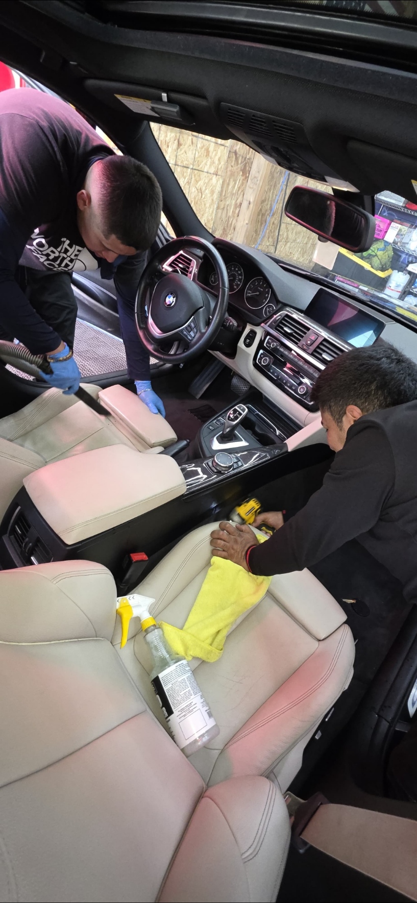 Two detailers cleaning the interior seats of a BMW